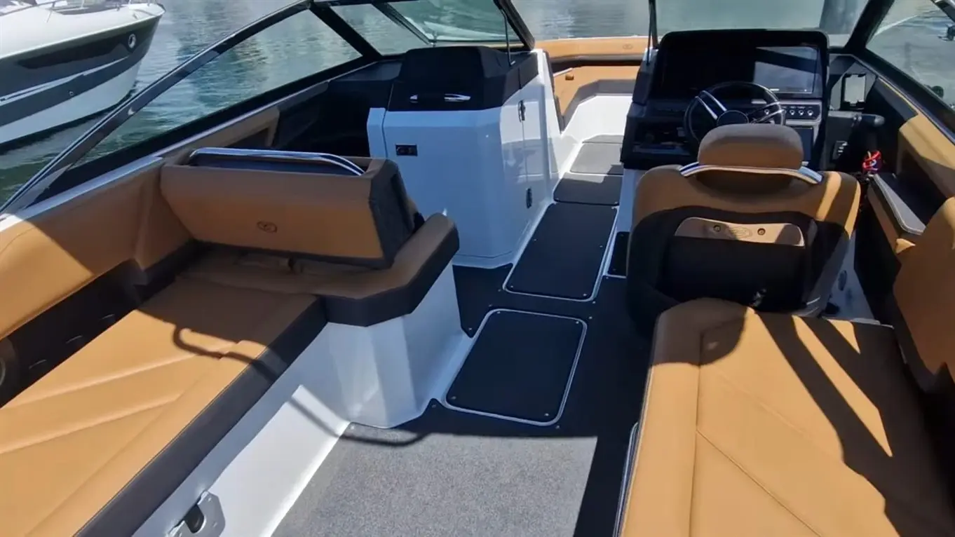 Interior of a modern boat showcasing tan and black seating, a steering wheel, and a sleek console by the water.